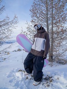 a man holding a snowboard standing in the snow next to some trees and bushes