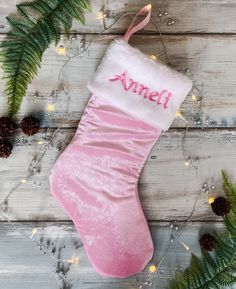 a pink christmas stocking with an embroidered name on it next to pine cones and greenery