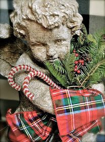 a statue of an angel holding a candy cane in its hand and wearing a plaid scarf around his neck