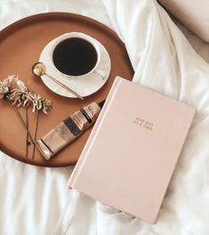 a cup of coffee next to a pink book on a bed