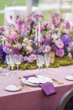 the table is set with purple and white flowers, gold place settings, and silverware