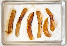 four pieces of bacon are on a baking sheet, ready to be cooked in the oven