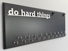 a sign that says do hard things hanging on the side of a wall with hooks attached to it