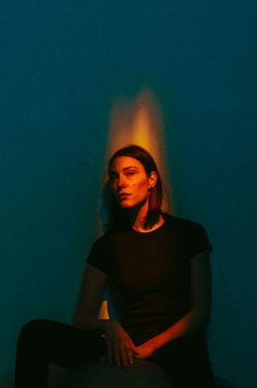 a woman sitting on the floor in front of a blue wall with light coming from behind her