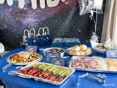 a blue table topped with plates and trays of food next to a space themed wall