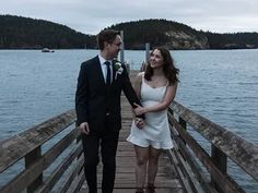 a man and woman standing on a pier next to the water