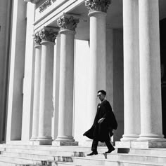 a man is walking down the steps in front of a building with columns and pillars