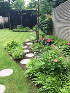 a garden with stepping stones in the grass and flowers on the side of the house