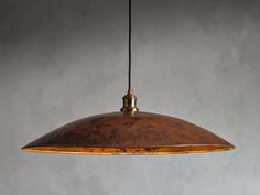 a large copper colored pendant light hanging from a metal ceiling fixture against a gray wall