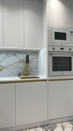 a kitchen with marble counter tops and white cabinets, gold trimming on the doors