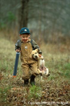 a little boy that is standing in the grass with a dog and holding a baseball bat