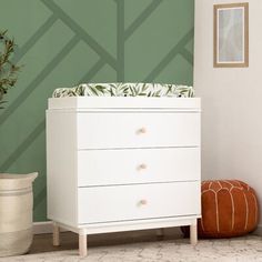 a white dresser sitting next to a green wall with a plant on top of it