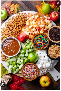 an assortment of fruits and nuts on a platter with chocolate, apples, pretzels, sprinkles