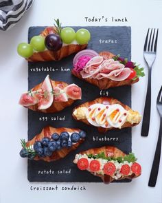 an assortment of food is displayed on a slate board with utensils and forks