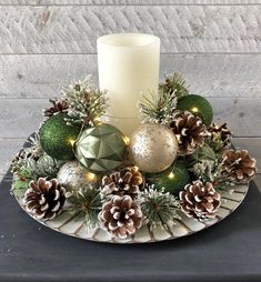 a white candle sitting on top of a plate with pine cones and christmas decorations around it