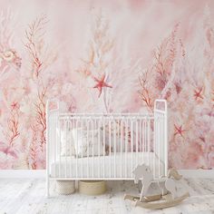 a white crib in front of a pink wall mural