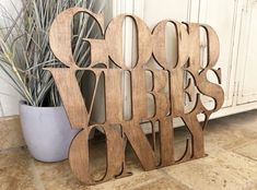 a wooden sign that says good vibes only on the floor next to a potted plant