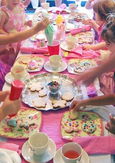 a group of children sitting around a table with cookies and teacups on it