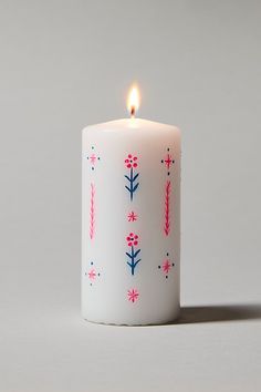 a white candle with red and blue designs on it's side next to a gray background