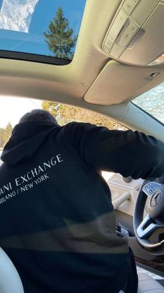 a man sitting in the driver's seat of a car wearing a hoodie