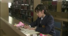 a young woman sitting at a table in front of a book shelf filled with books