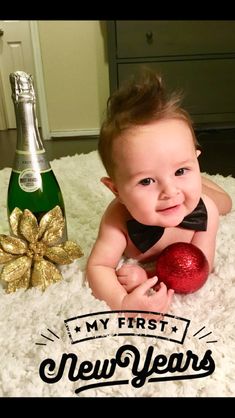 a baby laying on top of a white rug next to a bottle of champagne and a christmas ornament