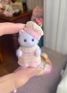 a small white cat wearing a pink hat and sweater on it's head is held in someones hand