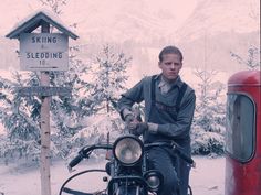 a man sitting on top of a motorcycle next to a red gas pump and sign