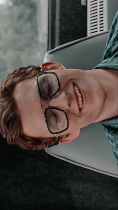 a young man wearing glasses sitting in front of a window with his head tilted to the side