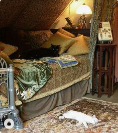 a cat laying on top of a bed next to a night stand and lamp in a room