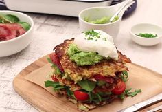 a stack of food sitting on top of a wooden cutting board next to bowls and utensils