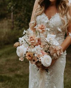 a woman in a wedding dress holding a bouquet of white and peach flowers with greenery behind her