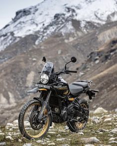 a black motorcycle parked on top of a grass covered field next to a snow covered mountain