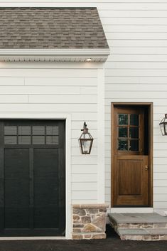 a white house with a black garage door and two lights on the side of it