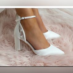 a woman's white high heeled shoes on top of a fluffy pink blanket