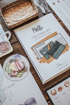 a table topped with notebooks and papers next to utensils on top of a wooden table