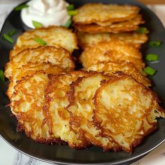 some fried food on a black plate with sour cream and green onions next to it