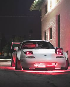 a white sports car parked in front of a building with its lights on at night