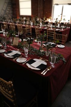 the table is set with black and white plates, silverware, greenery and place settings