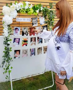 a woman standing next to a white easel with pictures on it and greenery