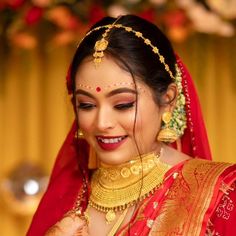 a woman in a red and gold bridal outfit smiles as she adjusts her jewelry