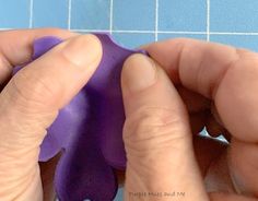 someone is making a paper flower out of purple construction material on a piece of blue tile