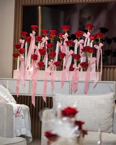 red roses are arranged in vases with pink ribbons on the table and behind them is a white couch