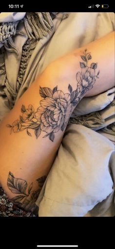 a woman laying on top of a bed covered in blankets and sheets with flowers tattooed on her arm