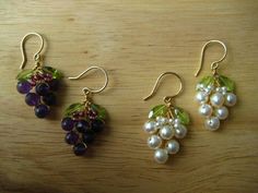 three pairs of earrings with grapes and leaves hanging from them on a wooden table top