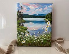 a painting of daisies by a lake with mountains in the background on a canvas