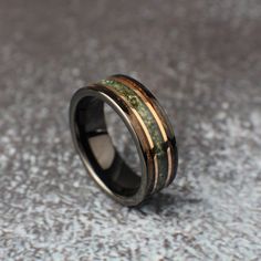 a wedding ring with gold and green inlays on the inside, sitting on a gray surface