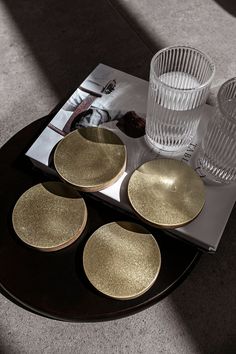 three gold plates sitting on top of a table next to two glasses and a magazine