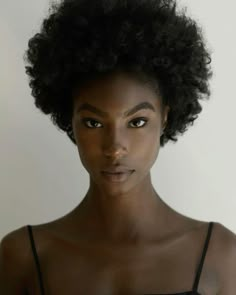 a woman with an afro looks at the camera while wearing a tank top and black bra