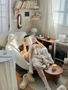 a woman sitting on a couch reading a book in her living room with white furniture